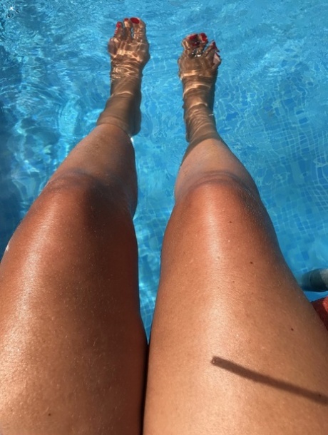 Mature woman Sweet Susi dips her painted toenails into a swimming pool 20349817